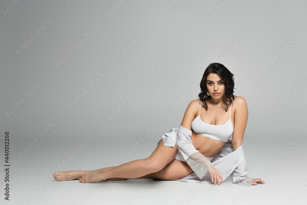 Fototapeta premium Barefoot woman in underwear and silk robe sitting on grey background
