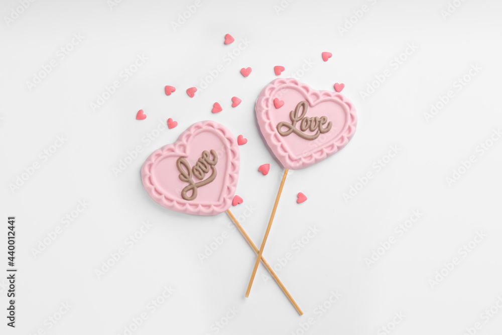 Chocolate heart shaped lollipops and sprinkles on white background, flat lay