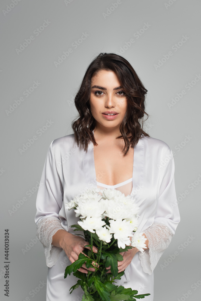 Smiling woman in satin robe holding flowers isolated on grey Smiling woman in satin robe holding flowers isolated on grey