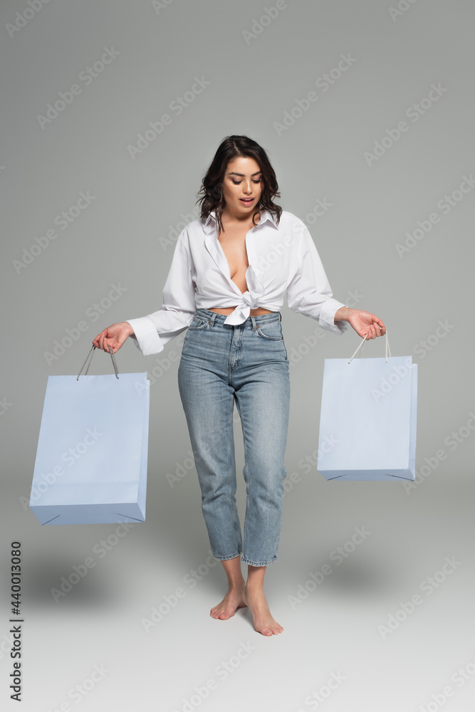 Excited and sexy woman looking at shopping bags on grey background Excited and sexy woman looking at shopping bags on grey background
