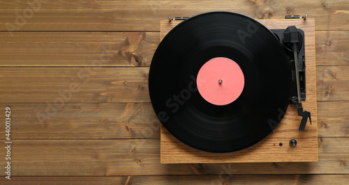 Turntable with vinyl record on wooden background, top view