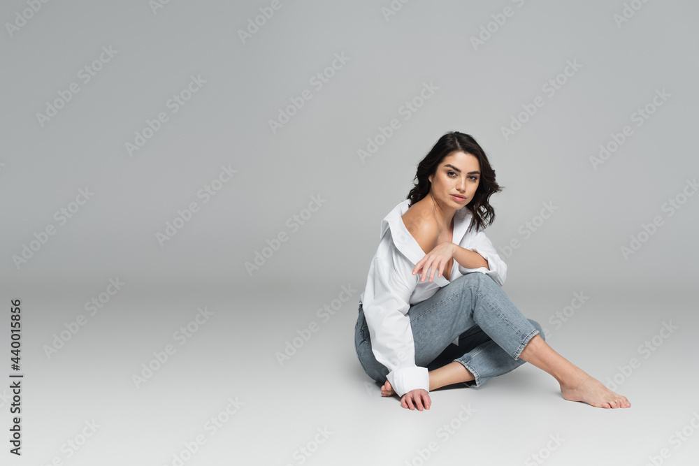 Young woman in jeans and shirt looking at camera on grey background Young woman in jeans and shirt looking at camera on grey background