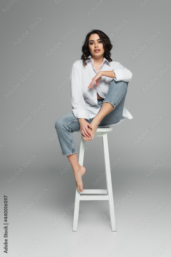 Smiling barefoot woman sitting on chair on grey background Smiling barefoot woman sitting on chair on grey background