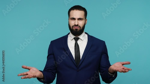Exhausted tired young man in formal black suit showing mind explosion gesture, feeling unhappy and nervous, lots unnecessary information. Indoor studio shot isolated on blue background.