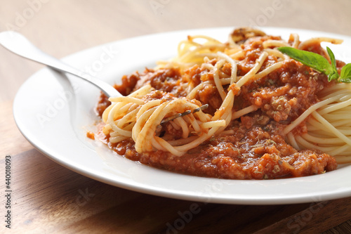 Close up a fork with spaghetti and red sauce in white dish on cutting board