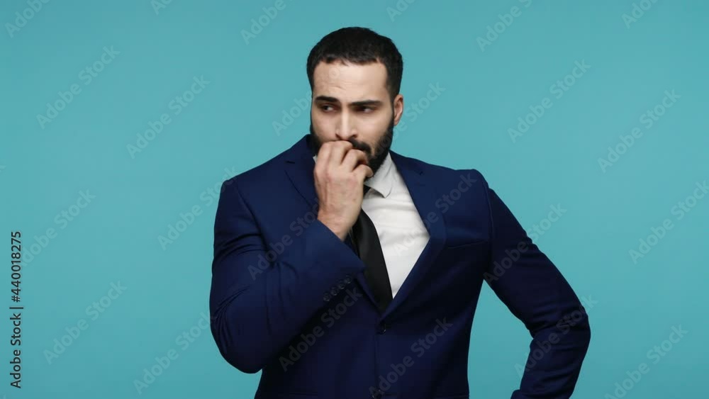 Worried bearded attractive man biting finger nails, feeling nervous, in anticipation of bad event, poses with gloomy face, is about to cry. Indoor studio shot isolated on blue background. Worried bearded attractive man biting finger nails, feeling nervous, in anticipation of bad event, poses with gloomy face, is about to cry. Indoor studio shot isolated on blue background.