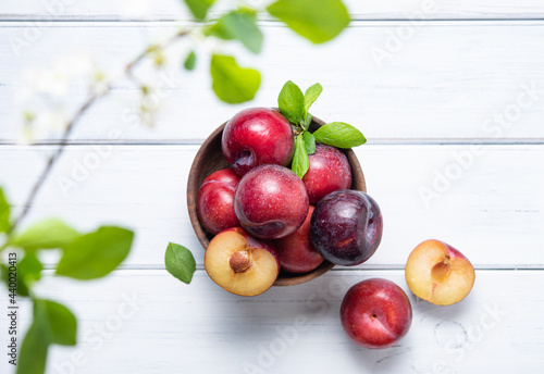 a few juicy and sweet red plums in bowl with green leaves on a white wood background. Top view and copy space