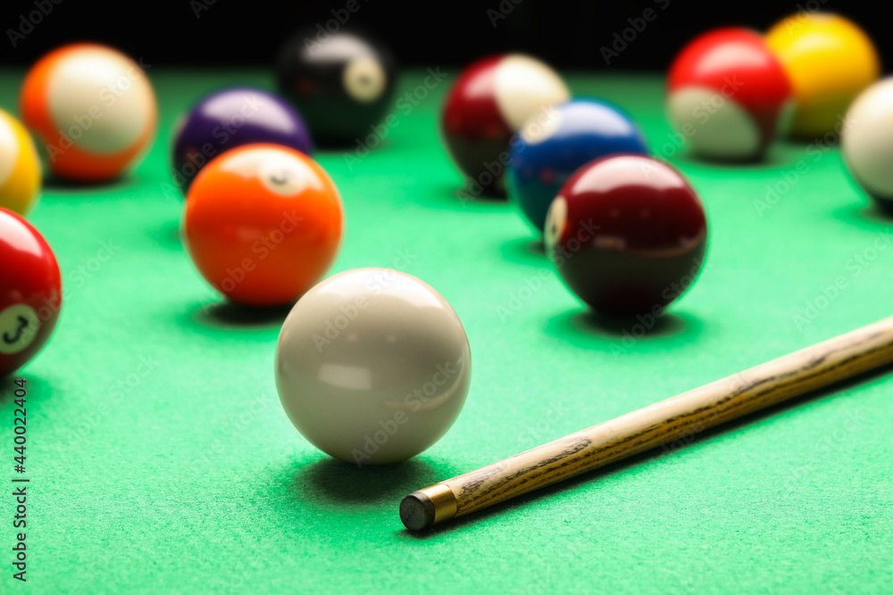 Many colorful billiard balls and cue on green table