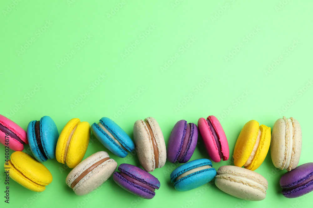 Delicious colorful macarons on green background, flat lay. Space for text Delicious colorful macarons on green background, flat lay. Space for text