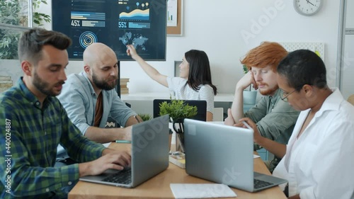 Young woman is making presentation speaking and pointing at digital board then throwing paper balls at unattentive employees in office. Business and lifestyle concept. photo