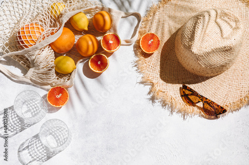 Summer fashion flat lay on white background. Holiday party, vacation, travel, tropical concept. Straw hat, sunglasses, glass and citrus fruits. Palm shadow and sunlight, sun. Top view, copy space. photo