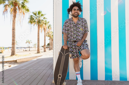 Afro Latin man having fun listening music with headphones on tropical beach during vacations time