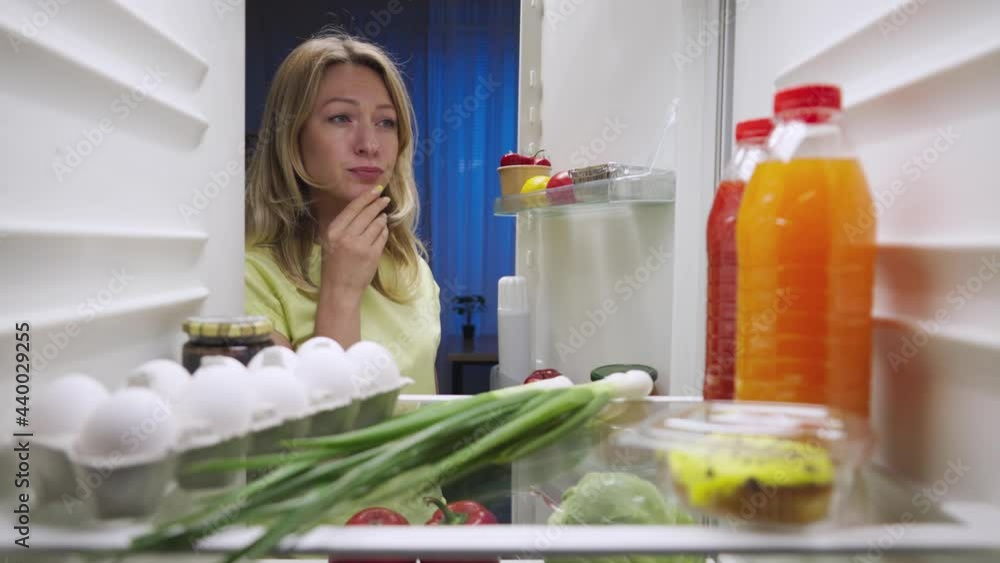 Sleepy young woman opens the refrigerator door at night, looks inside and picks out orange juice. View from inside the kitchen fridge. Close up. Slow motion ready 59.94fps. Sleepy young woman opens the refrigerator door at night, looks inside and picks out orange juice. View from inside the kitchen fridge. Close up. Slow motion ready 59.94fps.