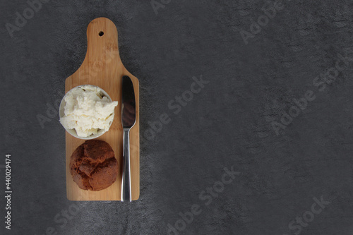 a bun, knife and a bowl of cheese on cutting board on gray background flat lay