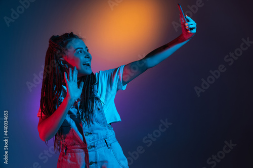 Caucasian young woman with phone isolated on blue studio background in neon. Concept of human emotions, facial expression.