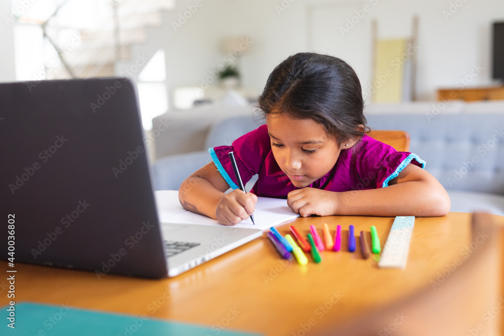 Happy hispanic girl sitting at kitchen table doing school work using laptop Happy hispanic girl sitting at kitchen table doing school work using laptop