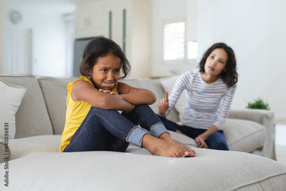 Sad hispanic daughter sitting on couch being told off by mother Sad hispanic daughter sitting on couch being told off by mother