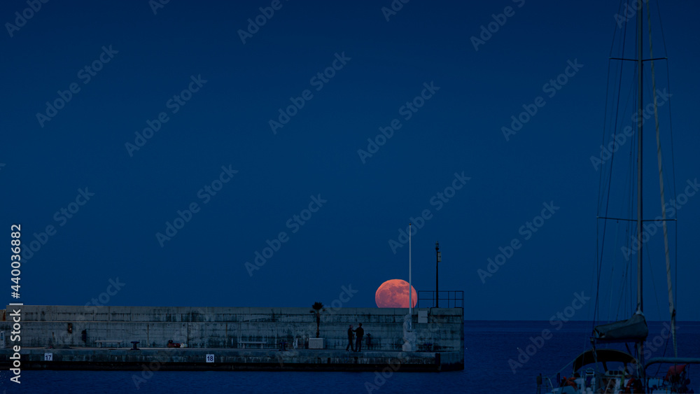 Obraz premium Roter Vollmond über dem Wasser in Hafenanlage