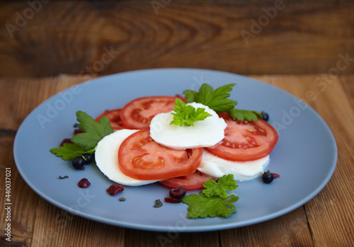 Italian caprese salad with sliced tomatoes, mozzarella, basil, olive oil on a wooden background.