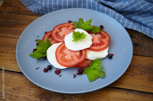 Italian caprese salad with sliced tomatoes, mozzarella, basil, olive oil on a wooden background.