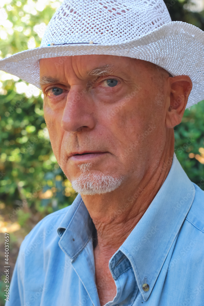 Close-up portrait of man with white hat, goatee and blue shirt in a public park