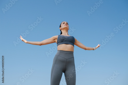 Majestic young woman in sportswear greetng the sun. Over blue sky © zzzdim