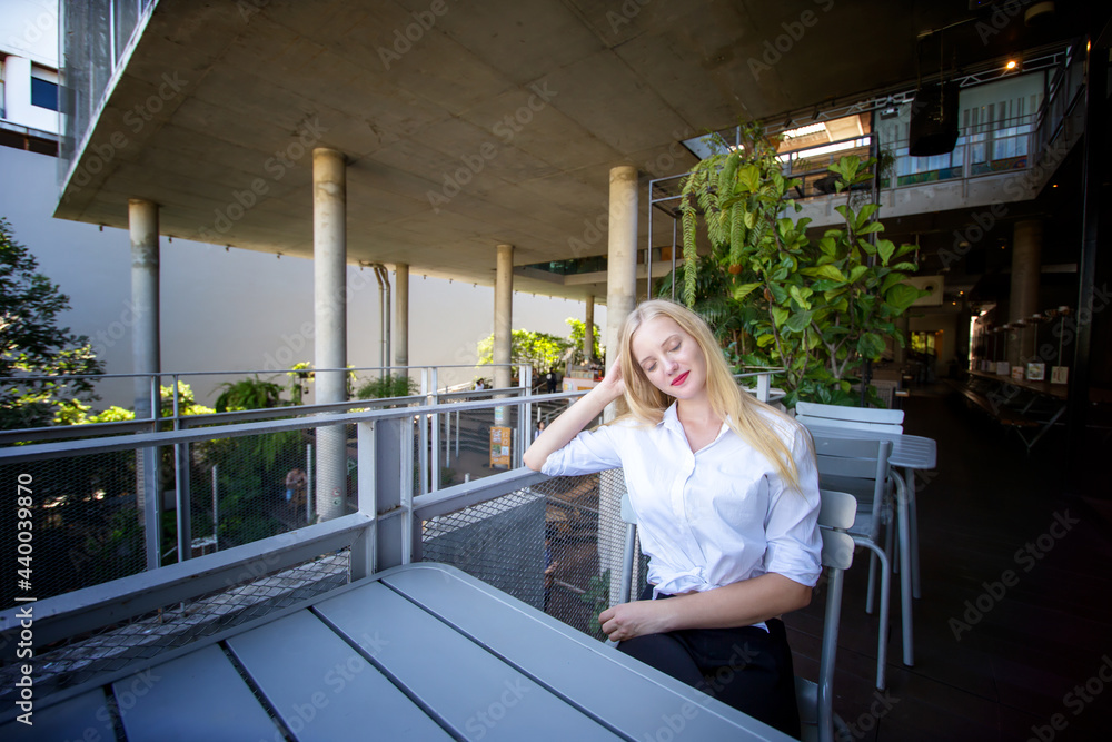 portrait of a beautiful fashion girl with blonde hair in a white shirt  sitting on café outside.