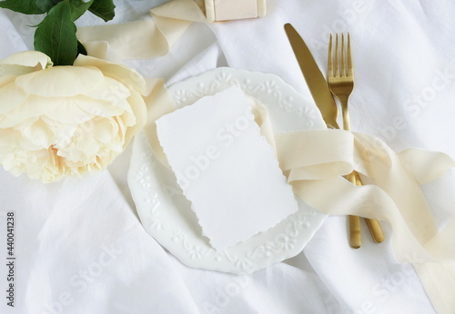 card mockup and cream peony flower on white plate on linen fabric background ...