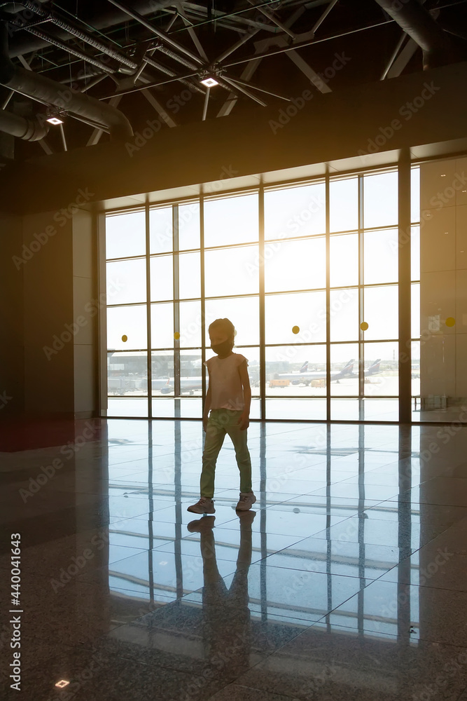 girl in medical mask walks through empty waiting room at airport. Large window illuminated by sun with view of airplanes preparing to take off girl in medical mask walks through empty waiting room at airport. Large window illuminated by sun with view of airplanes preparing to take off