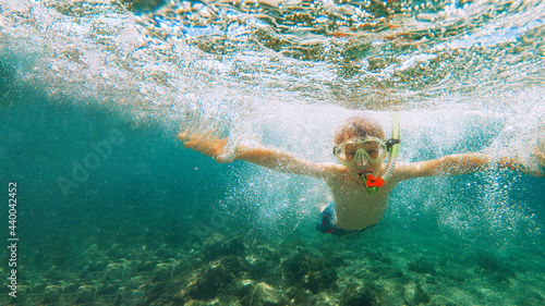 a child in a diving mask sits on the shore of the sea