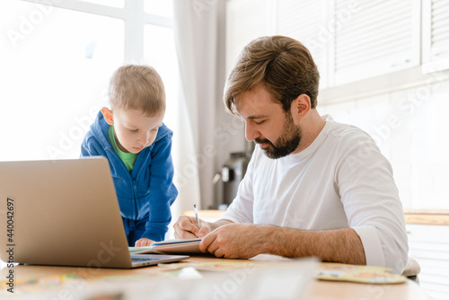 White father and son drawing and using laptop in kitchen at home