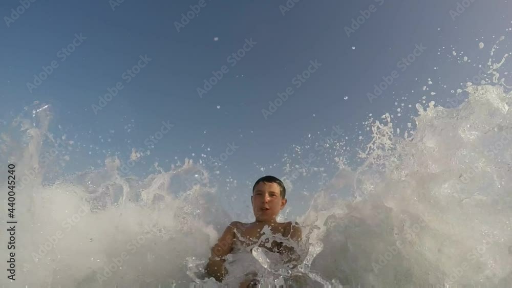 Smiling boy is waiting for a large sea wave to break on the sea shore