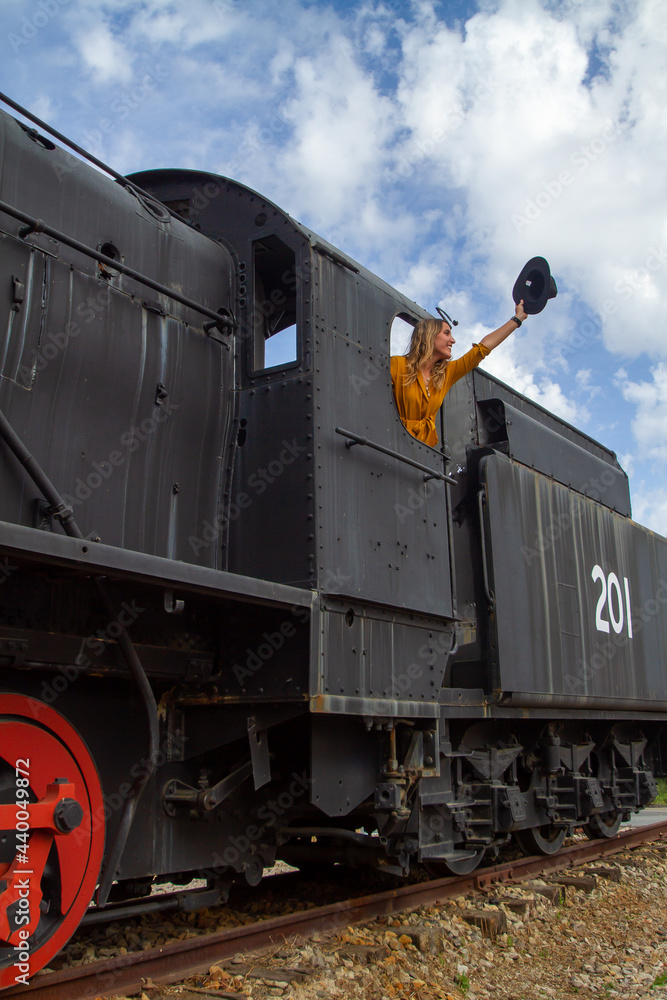 Naklejka premium young Spanish blonde woman with a yellow dress and a black hat in an old train station