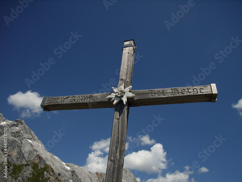 Ein Gipfelkreuz vor einer Bergwand und blauem Himmel