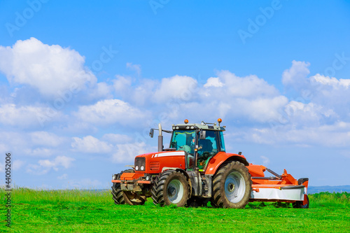 Large red tractor with a mower mows the grass on a field on a sunny day