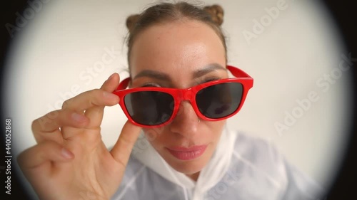 A young woman in white raicoat knocking on the door and looking through peephole