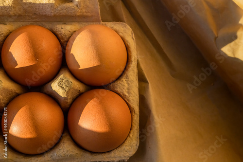 Obraz na plátně Four organic rustic brown golden eggs glowing yellow orange in the light of the sunset sun in a cardboard on kraft shining paper, carton box from the store