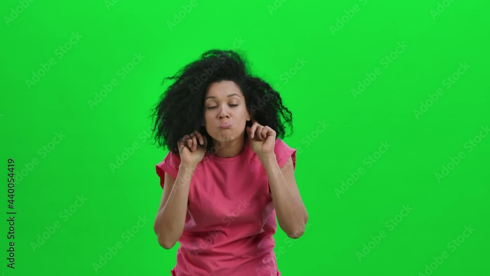 Portrait of young female African American posing for camera making funny faces. Black woman with curly hair poses on green screen in the studio. Close up. Slow motion ready 59.97fps. Portrait of young female African American posing for camera making funny faces. Black woman with curly hair poses on green screen in the studio. Close up. Slow motion ready 59.97fps.