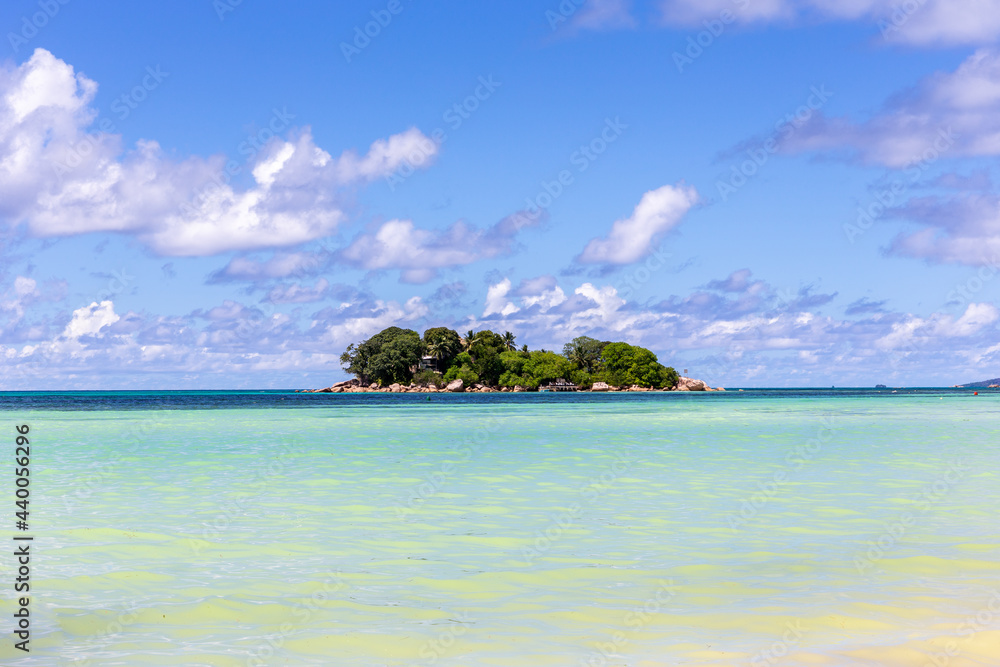 Uninhabited tropical island Chauve Souris protruding from Indian Ocean, with turquoise water around and crystal blue sky seen from Cote d'Or beach on Praslin, Seychelles.