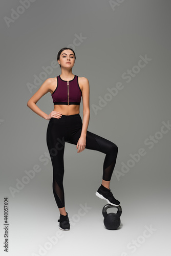 confident sportswoman stepping on kettlebell on grey background.