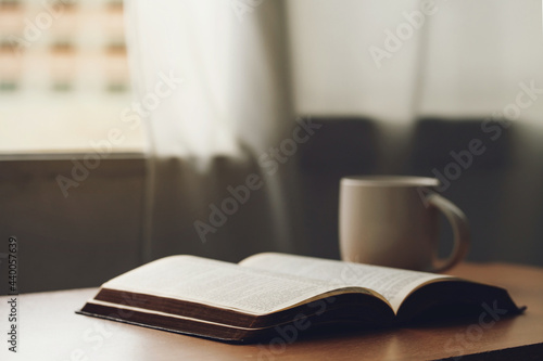 Fotografia Open bible with a cup of coffee for morning devotion on wooden table with window light