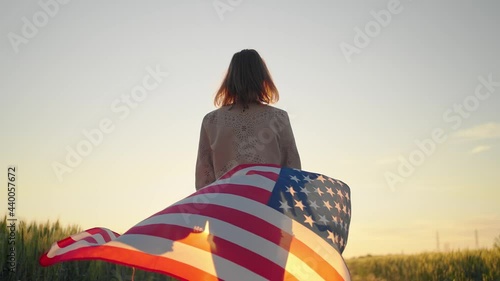 slow motion rear view of young beautiful sexy american woman holding a American flag walking wheat field at sunset photo