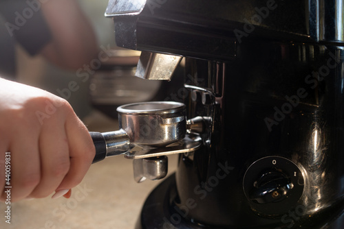 close-up of a barista holding a coffee portafilter. Electric coffee grinder in the coffee shop. The concept of the process of preparing beans for the preparation of aromatic espresso.
