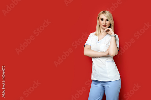 Obraz na płótnie Confident female doctor standing on red background. Young woman intern in medical clothes posing. w salonie