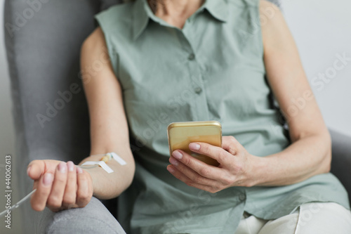 Foto Minimal close up of unrecognizable woman getting IV drip and using smartphone, c