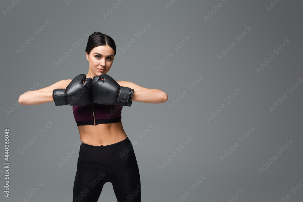 young sportswoman in boxing gloves looking at camera isolated on grey. young sportswoman in boxing gloves looking at camera isolated on grey.