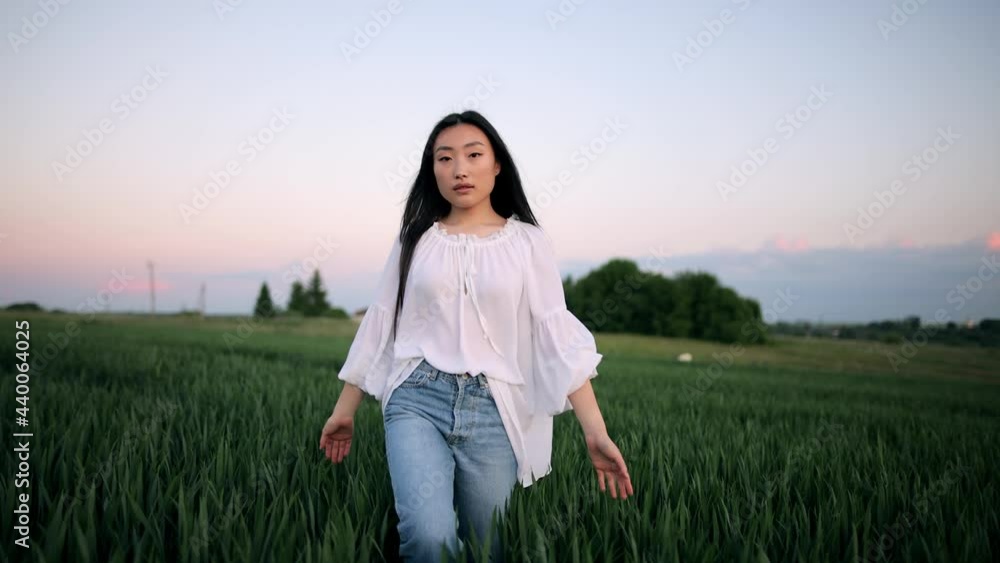 Young asian girl happily walking in slow motion through a field touching with hand wheat ears. Beautiful carefree woman enjoying nature and sunlight in wheat field at incredible colorful sunset Young asian girl happily walking in slow motion through a field touching with hand wheat ears. Beautiful carefree woman enjoying nature and sunlight in wheat field at incredible colorful sunset