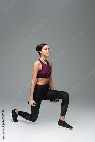 woman in black sportswear training with dumbbells on grey background.