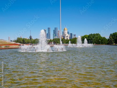 Jets of fountains on a sunny day against the backdrop of modern skyscrapers and a cloudless blue sky. Recreation area in Victory Park on Poklonnaya Hill in summer.