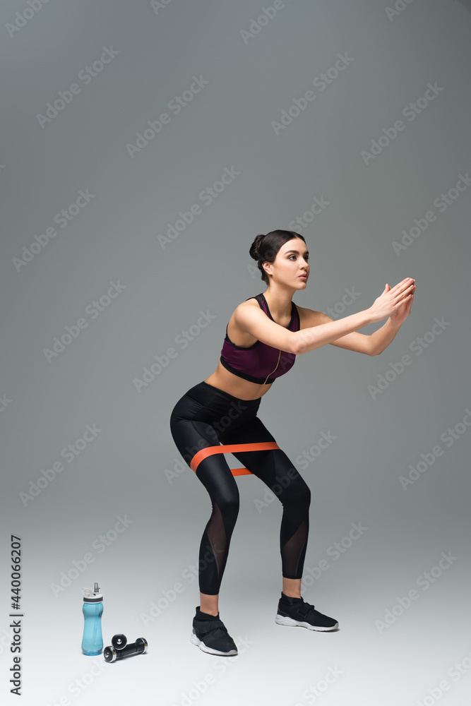 sportswoman doing sit ups with resistance band on grey background.